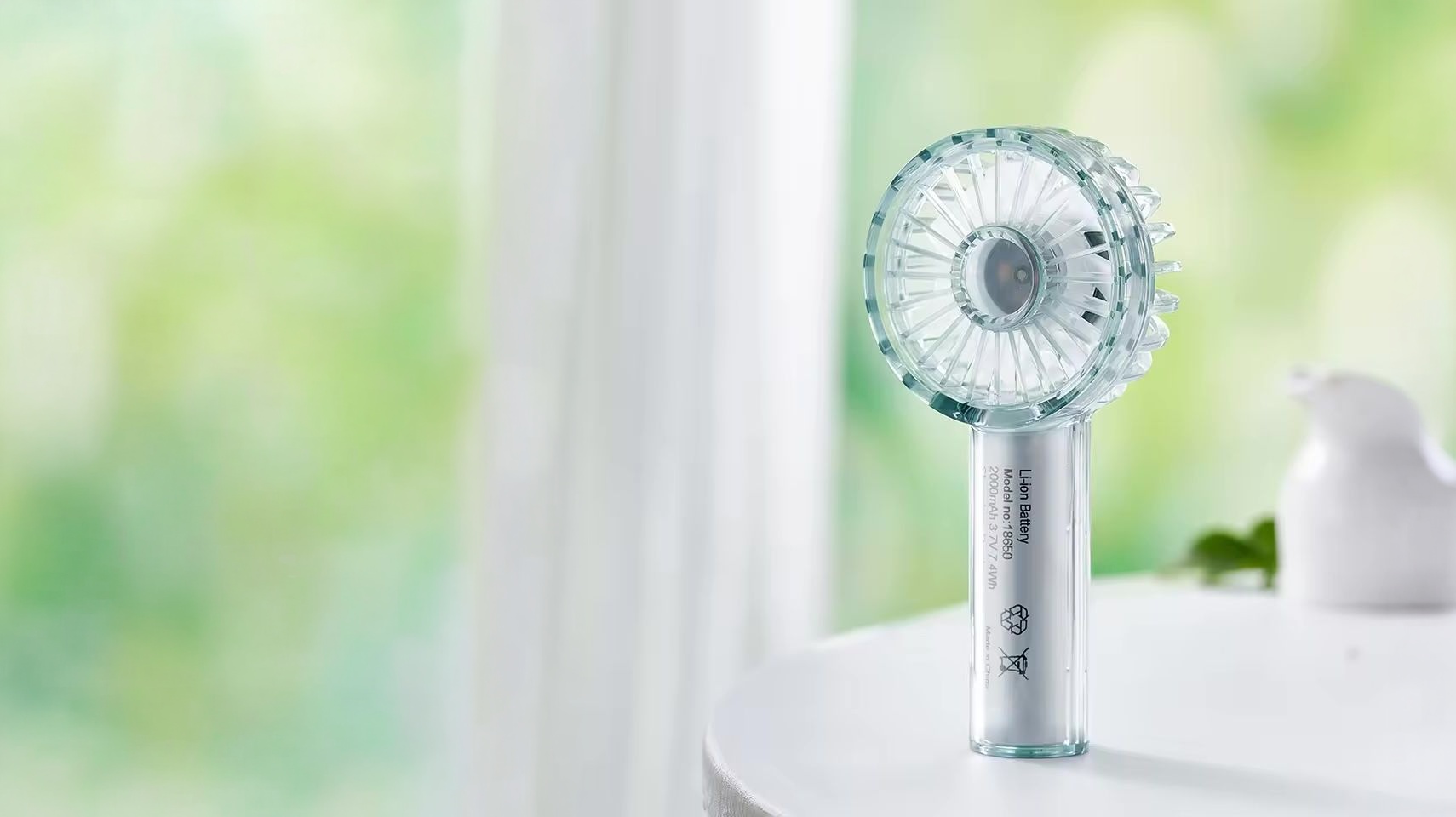窓辺の自然光の中に置かれた Clear Handy Mini Fan